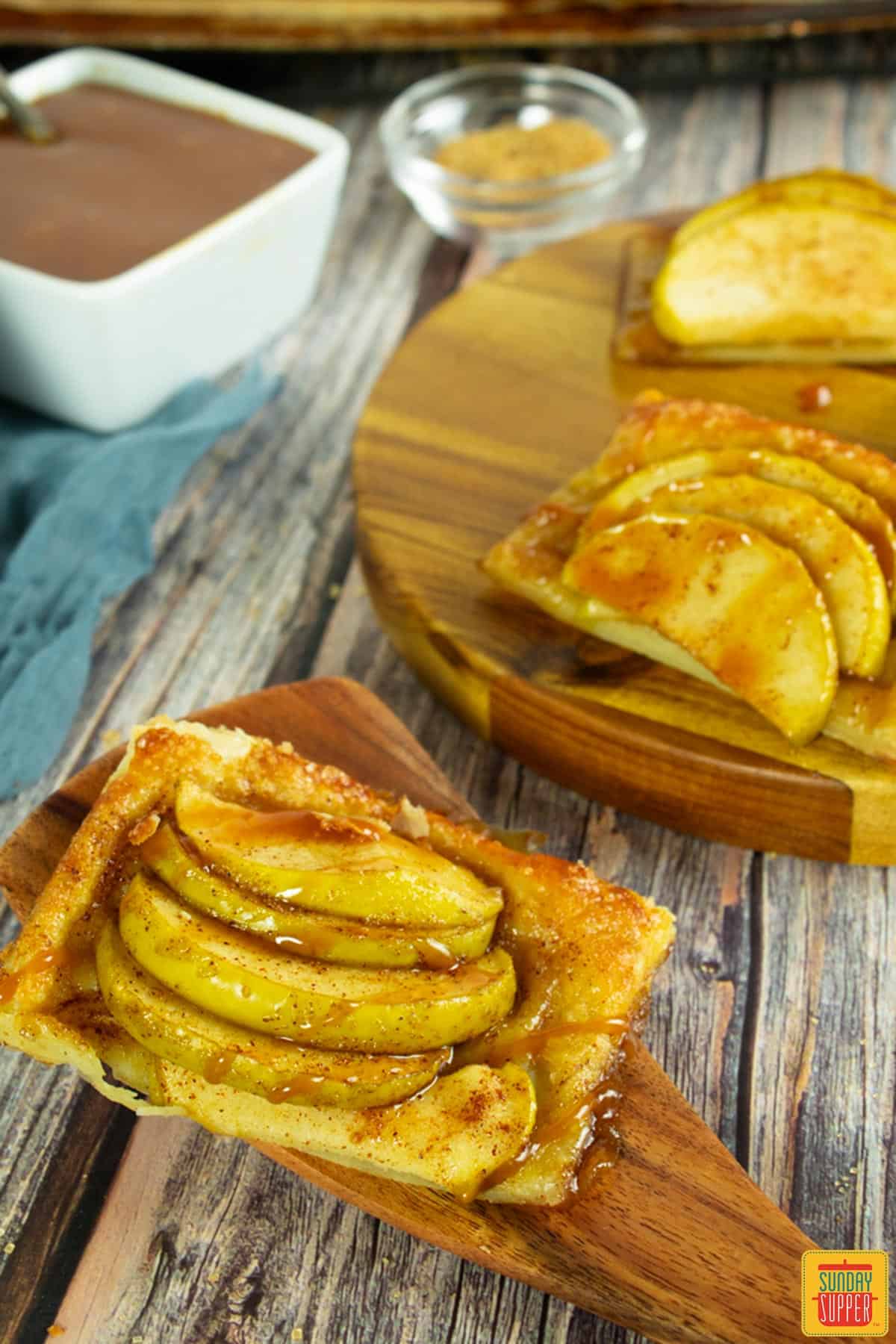 three apple tartlets, with two on a cutting board and one on a spoon
