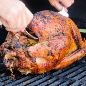 lifting a grilled turkey off of the grill