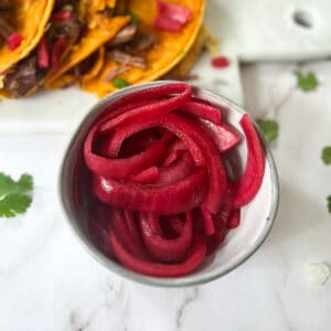 pickled red onions in a grey bowl with tacos behind