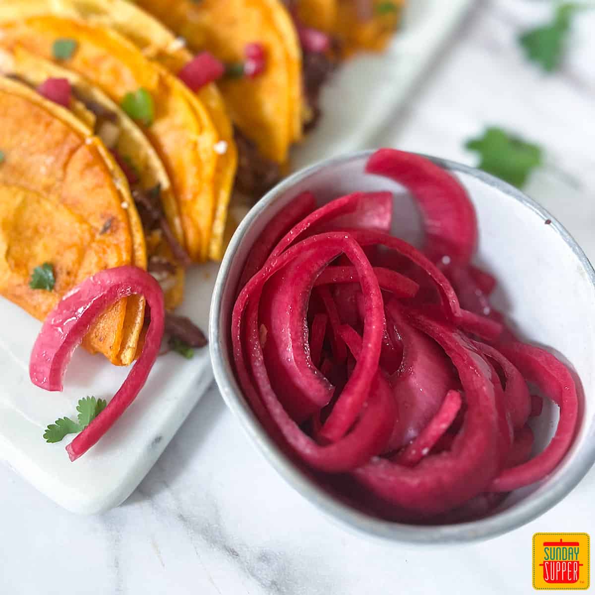 pickled red onions in a grey bowl with tacos behind