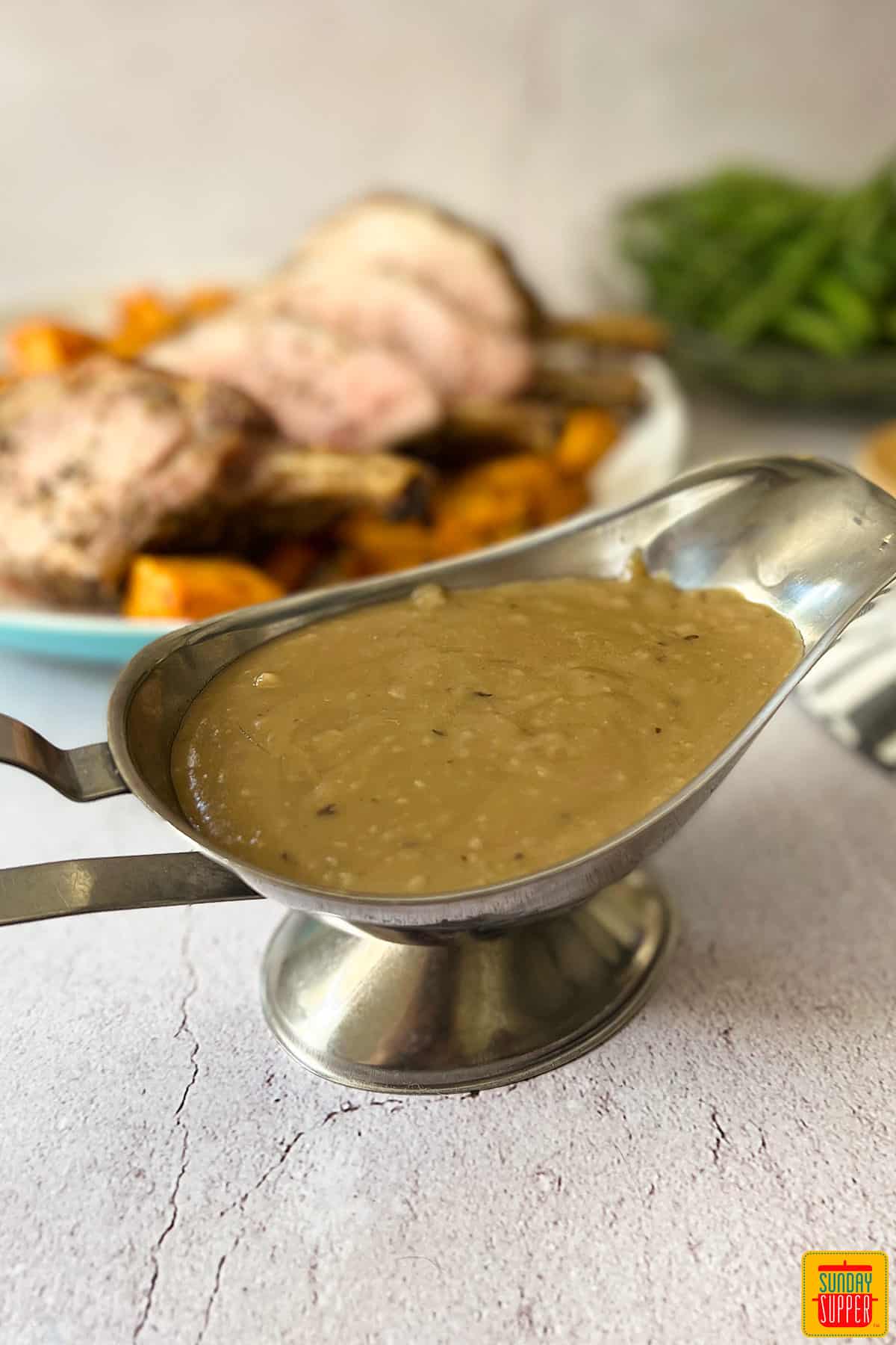 pork gravy in a metal gravy boat with pork behind