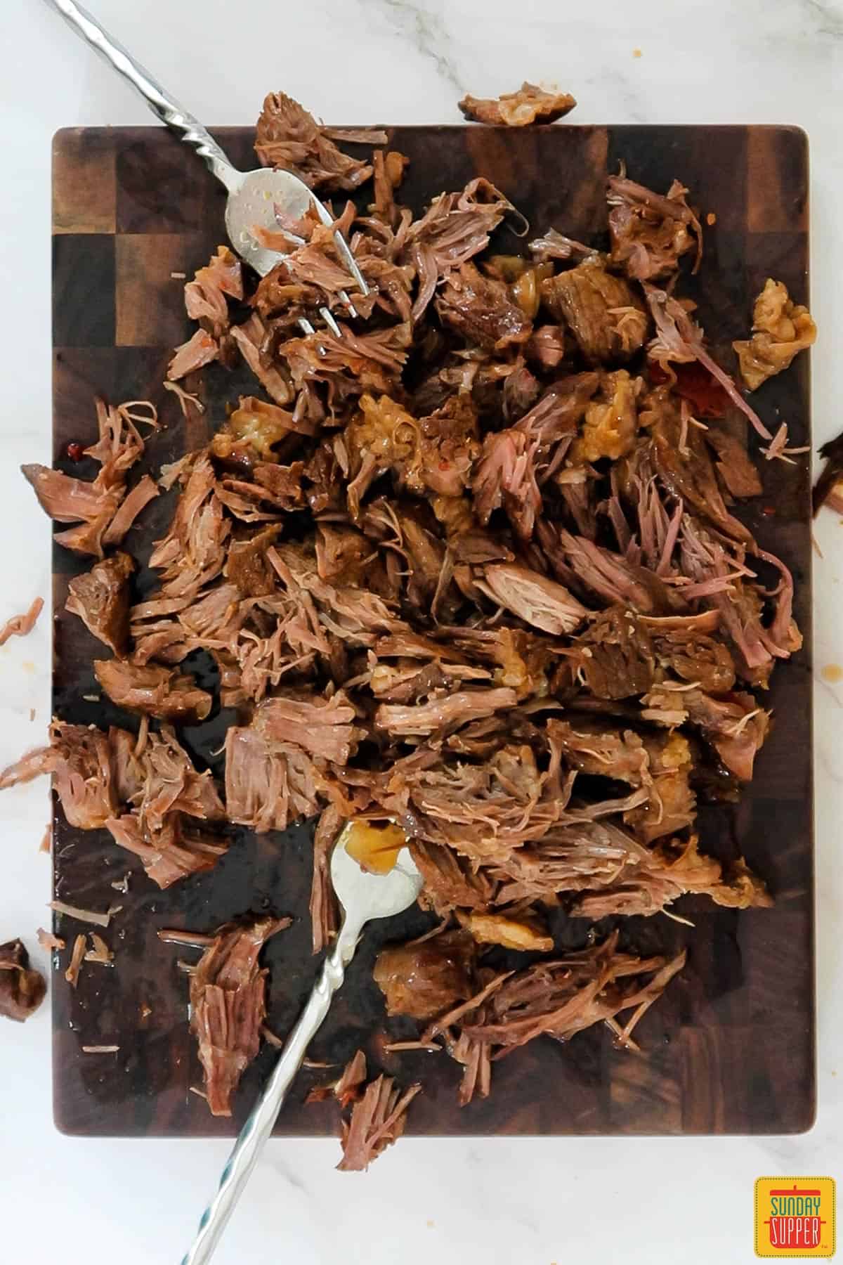 beef on a cutting board being shredded by two forks