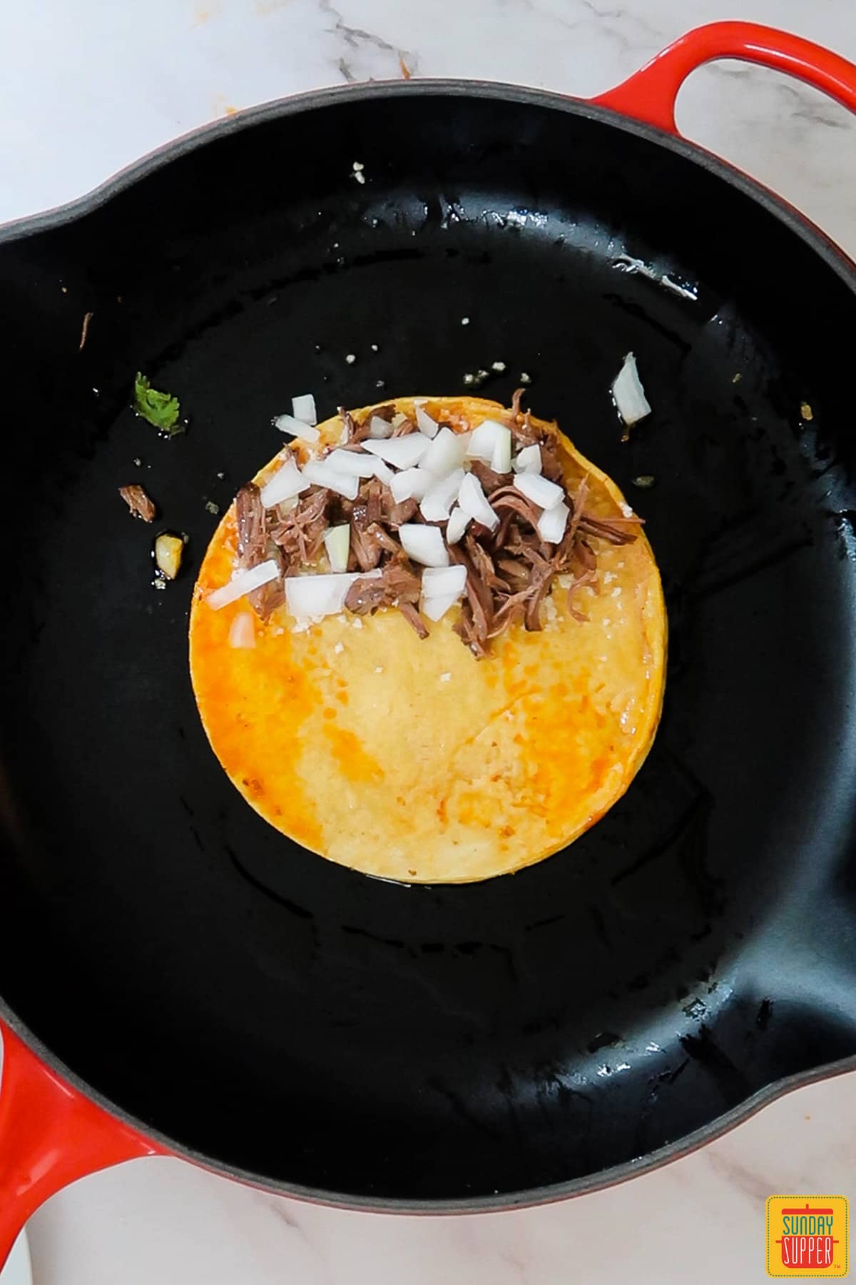 a black frying pan with an unfolded quesabirria taco filled with beef, cheese and onions in the center