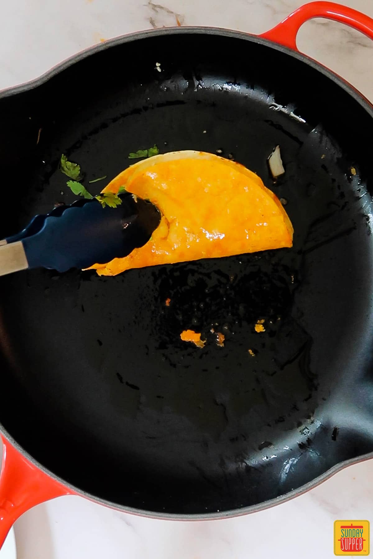 tongs flipping over a quesabirria taco on a black frying pan