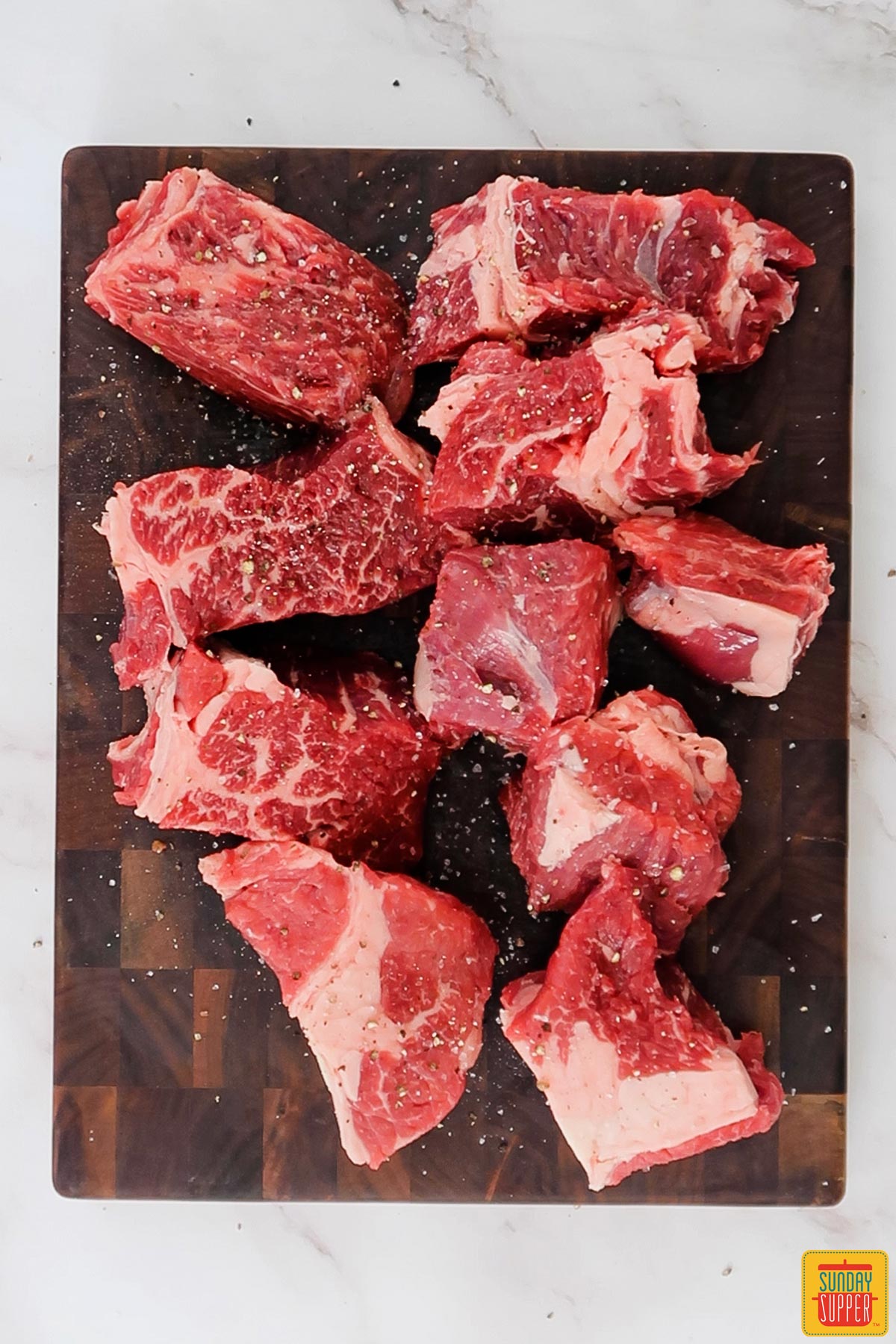 a cutting board covered in large chunks of raw beef that are sprinkled with salt and pepper