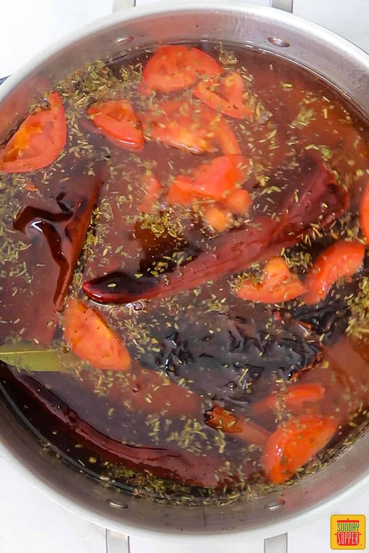 a pot with broth, seasonings and vegetables simmering