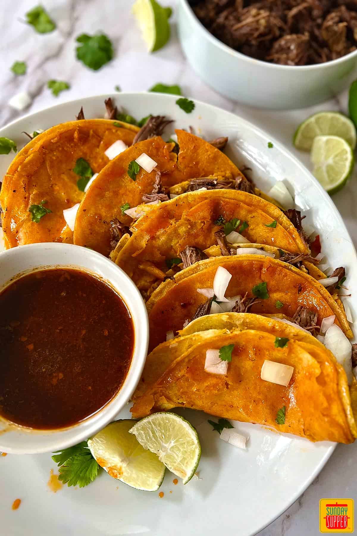 birria tacos on a plate with birria, limes, cilantro and onions