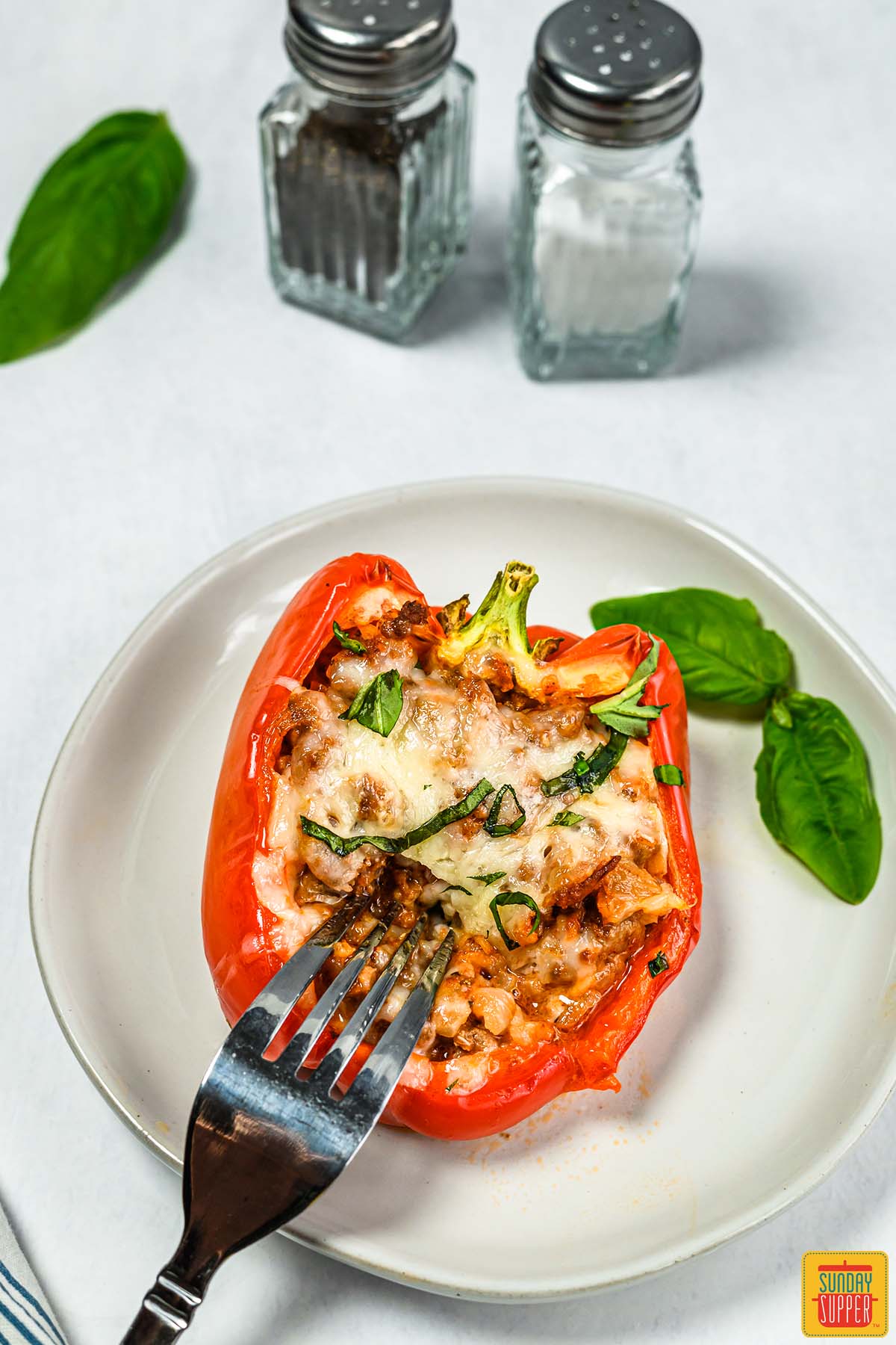 stuffed red bell pepper on a white plate with fresh basil and a fork