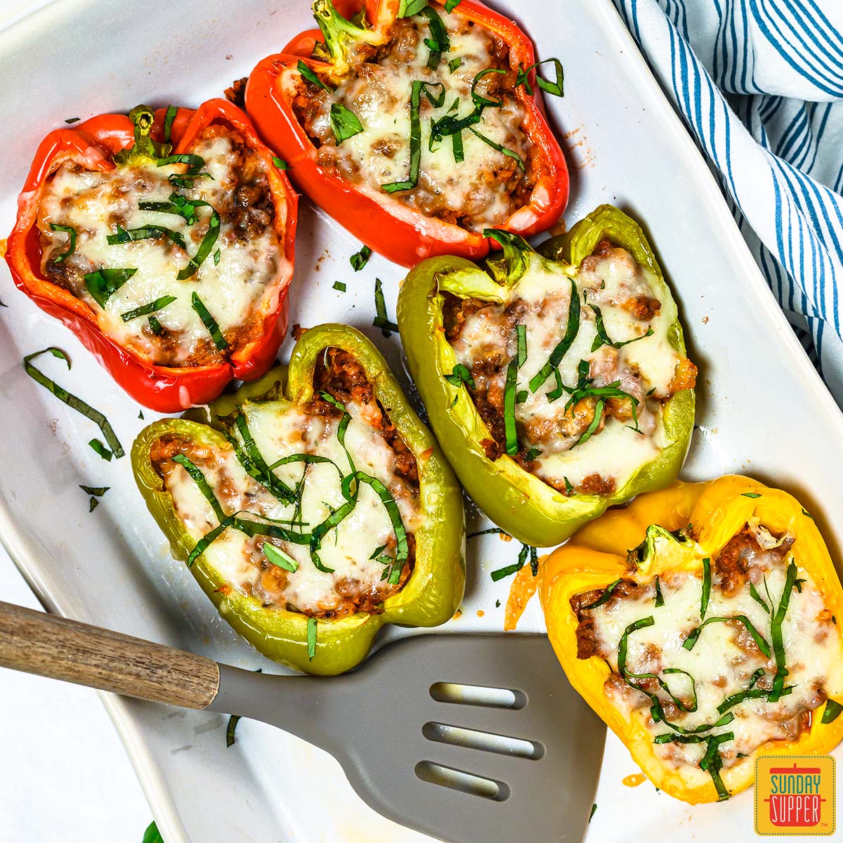 five stuffed bell peppers in a white dish with a spatula