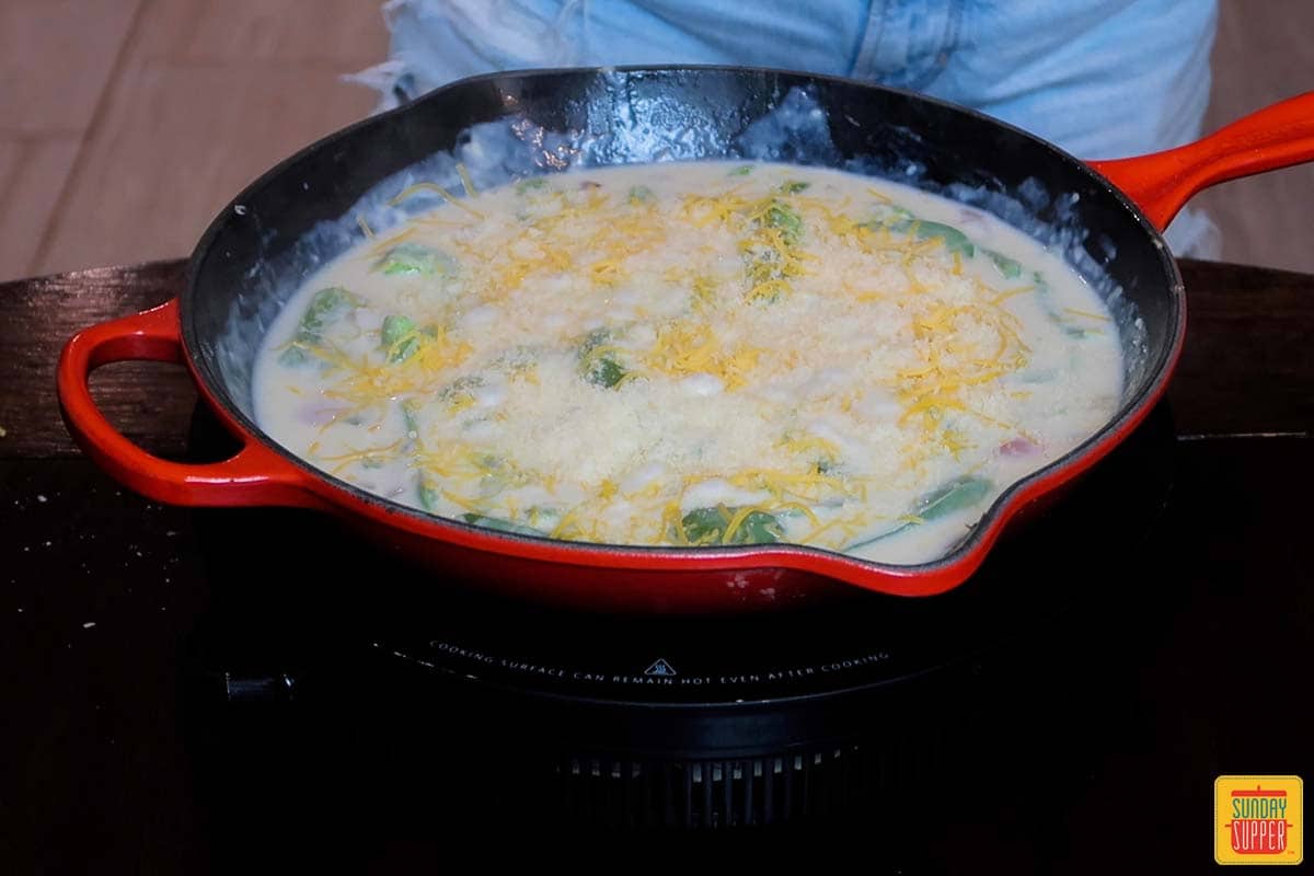 adding cheese to skillet with milk peppers and onions