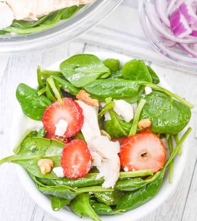 strawberry spinach salad in a white bowl with the rest of the salad behind