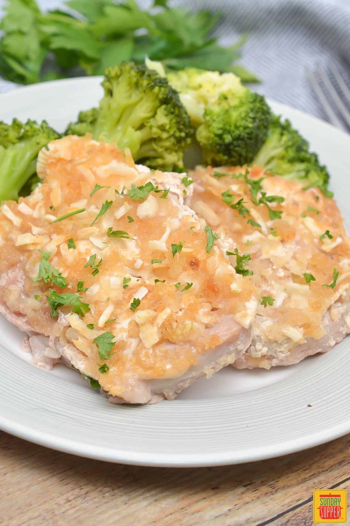 French onion pork chops on a white plate served with broccoli