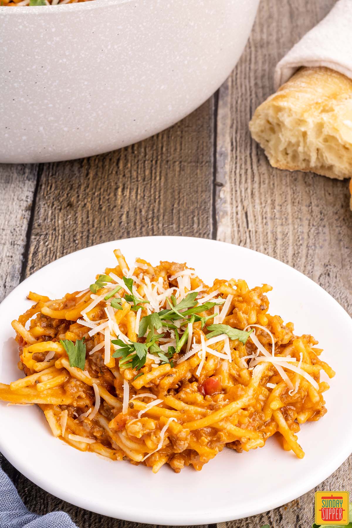 one pot spaghetti on a plate with parsley and cheese next to fresh bread