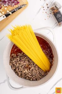 adding spaghetti noodles to pot with other ingredients