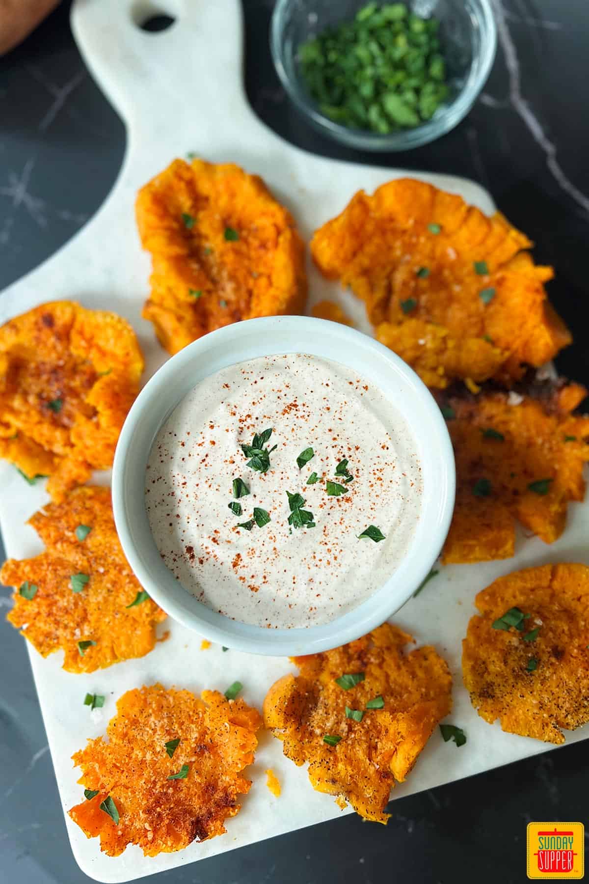 smashed sweet potatoes on a white marble cutting board with sauce in the middle