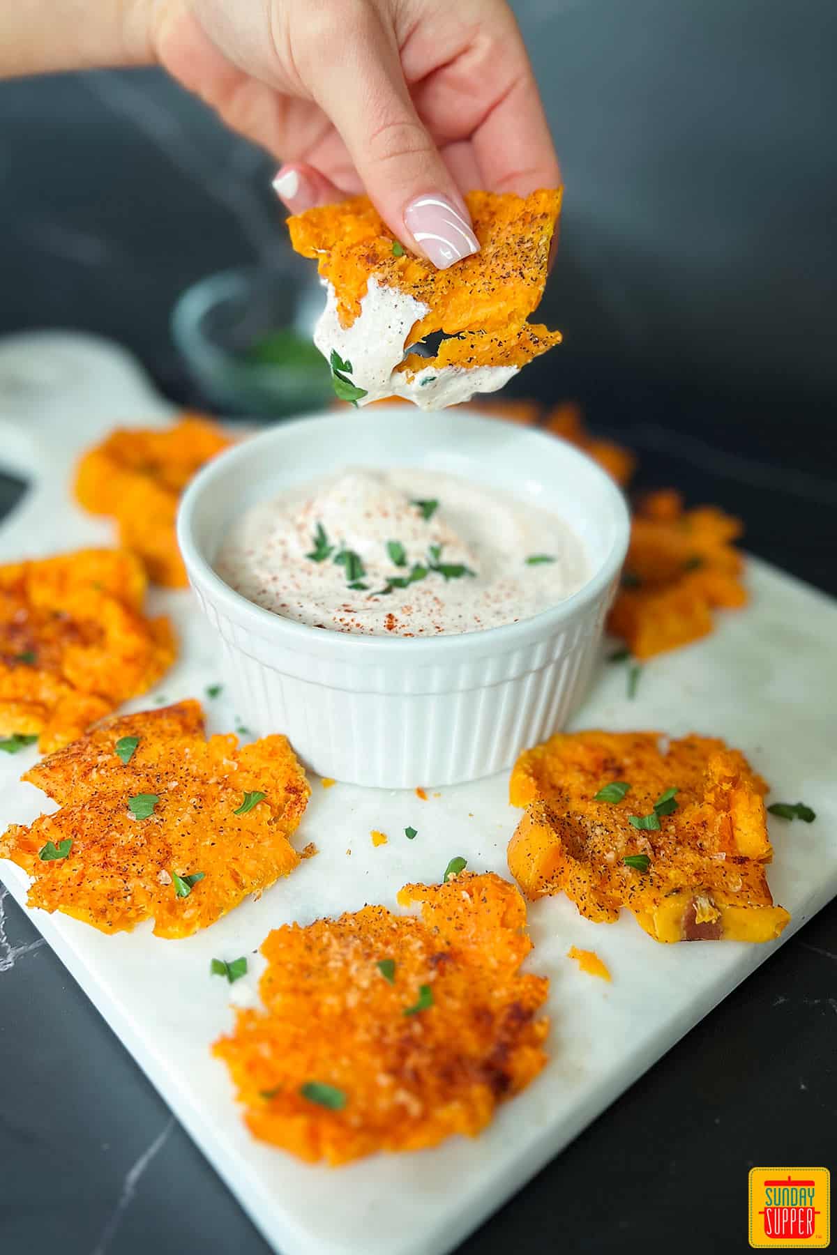 smashed sweet potatoes on a white cutting board dipping into sweet potato dipping sauce