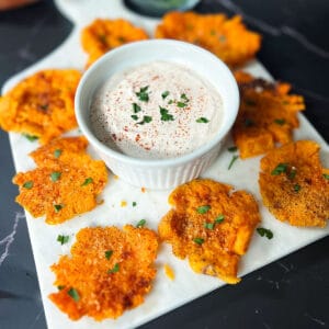 smashed sweet potatoes on a white cutting board with sweet potato dipping sauce in the center