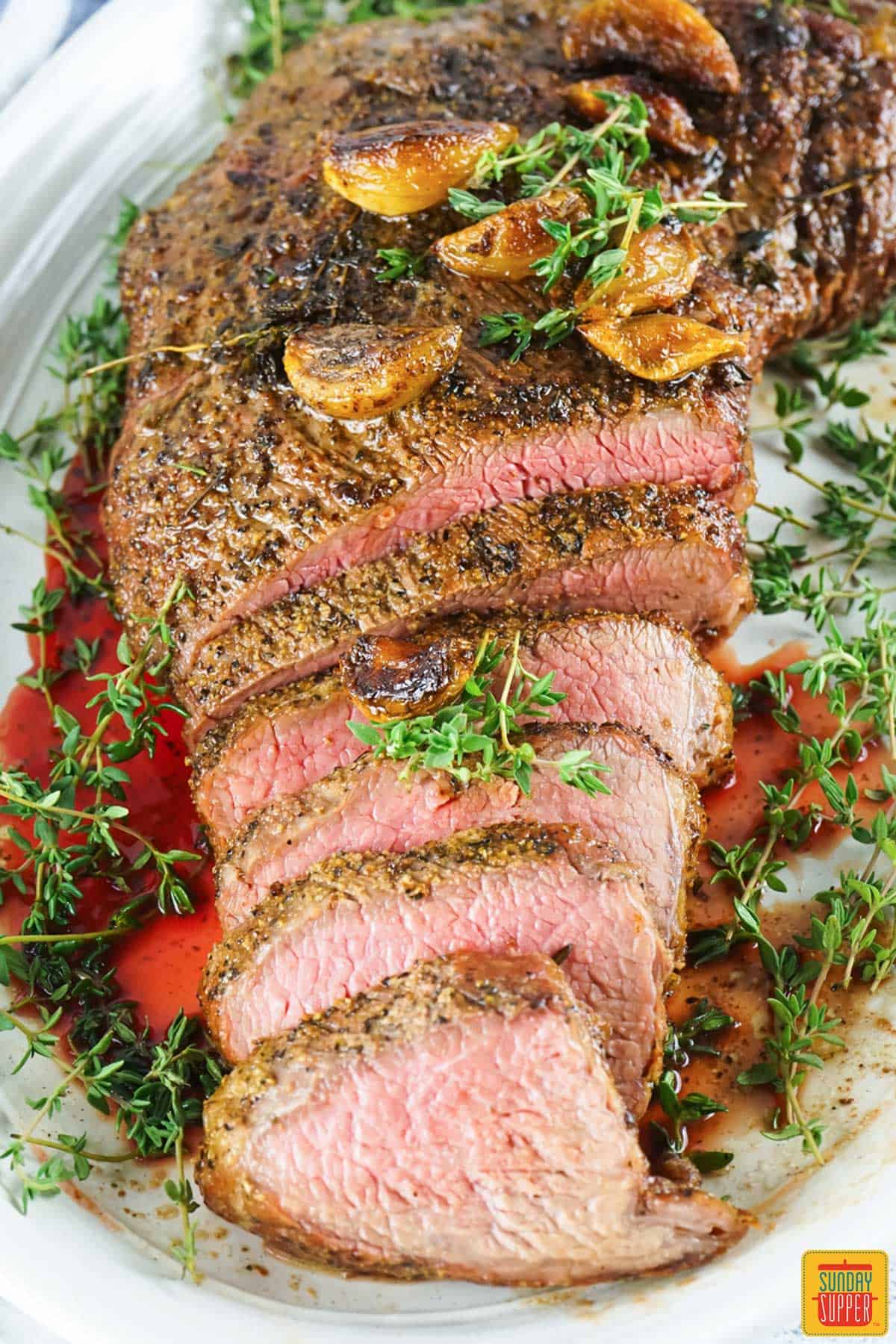 a line of sliced smoked tri tip on a plate in a pool of juices and thyme
