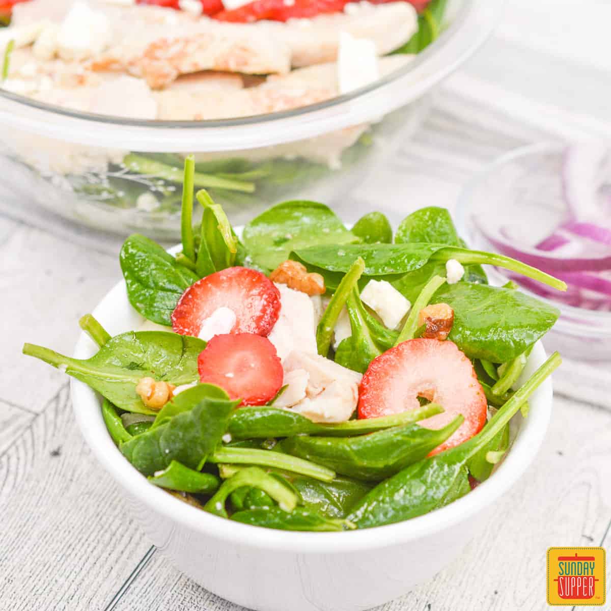 strawberry spinach salad in a white bowl with red onions in the background