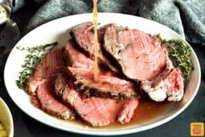 sliced prime rib on a white plate with au jus being poured on the slices