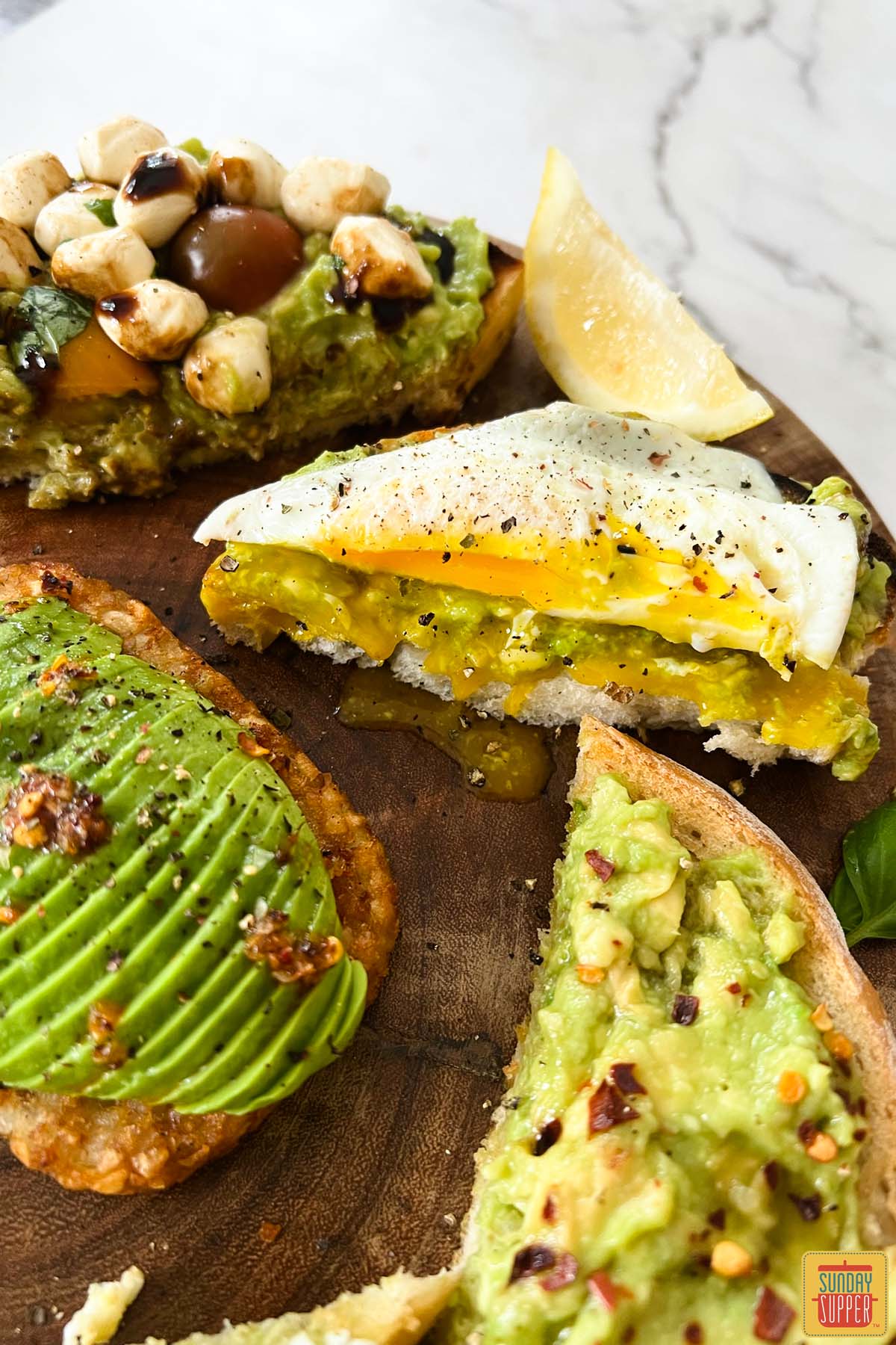 four different kinds of avocado toast on a wooden board