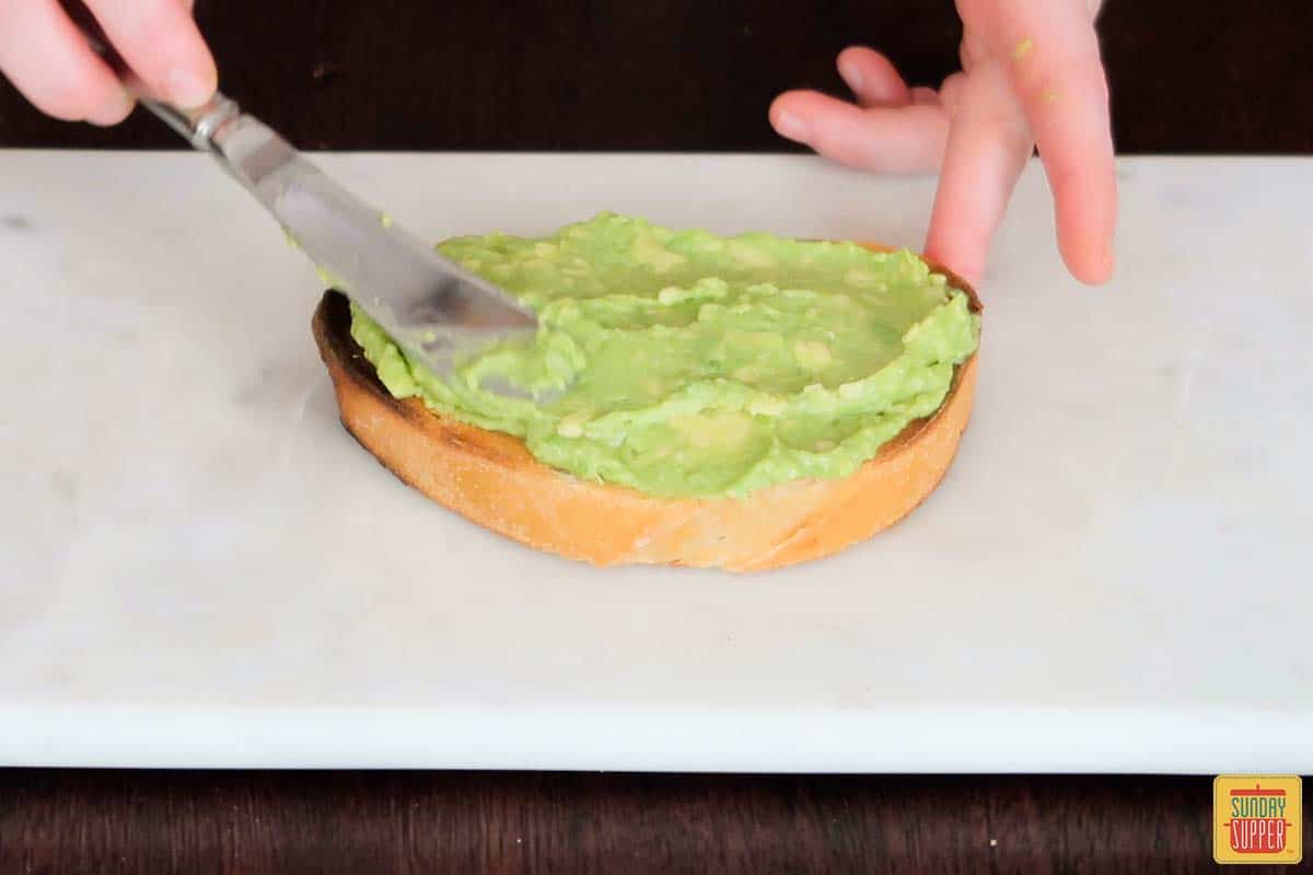 spreading mashed avocado on toasted bread with a knife