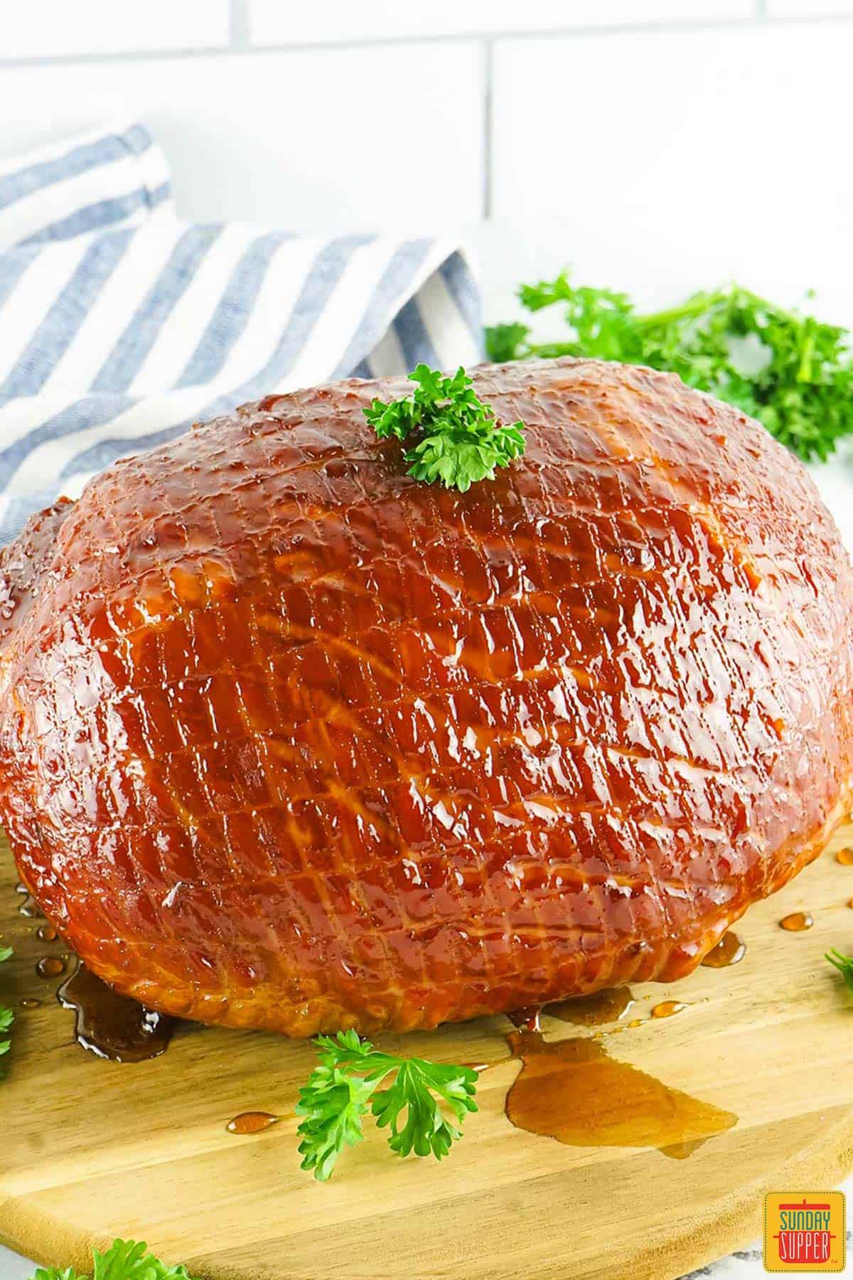 a fully cooked bourbon glaze ham on a wooden cutting board with parsley garnish