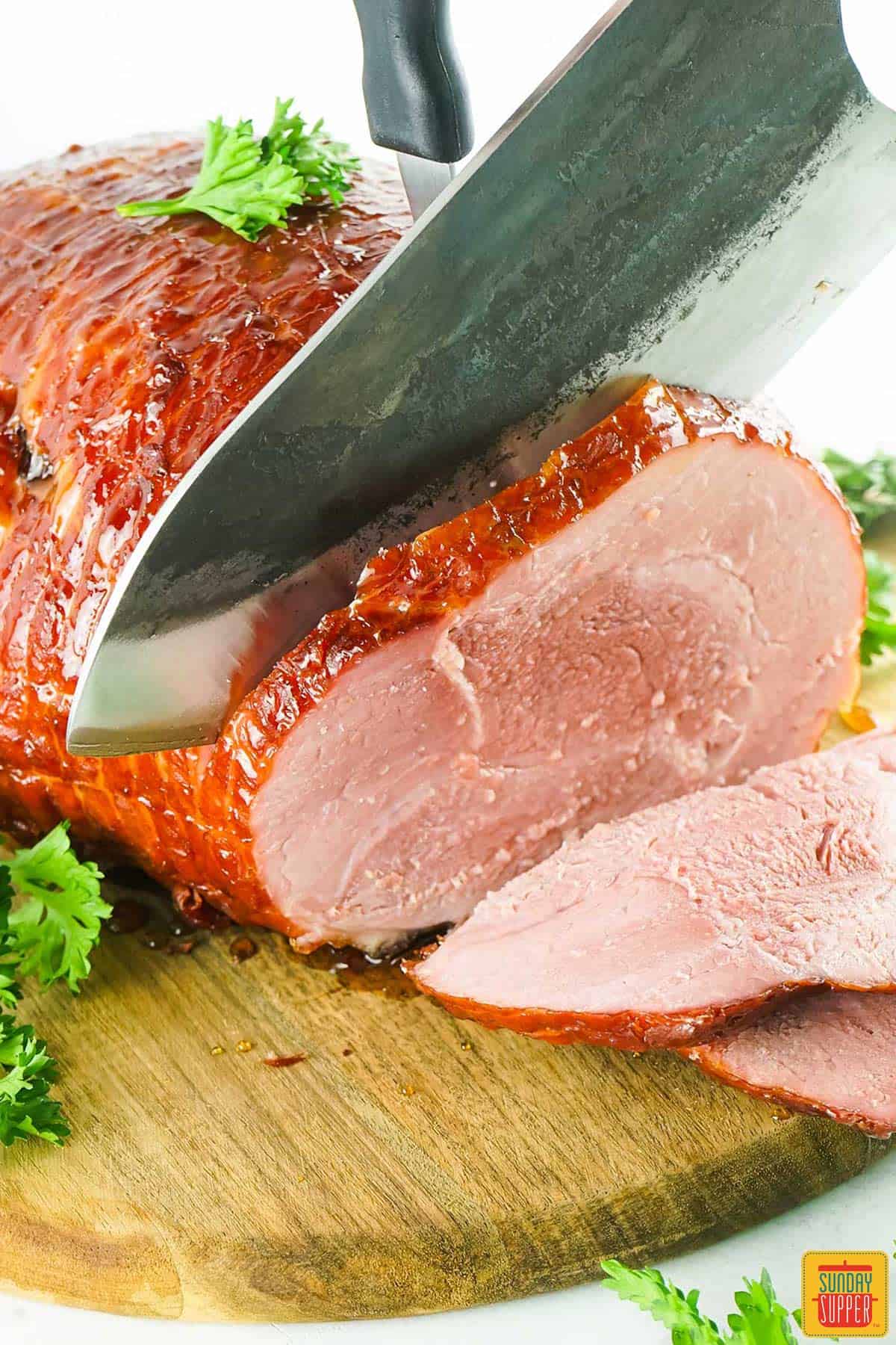 bourbon glazed ham being sliced on a cutting board with parsley