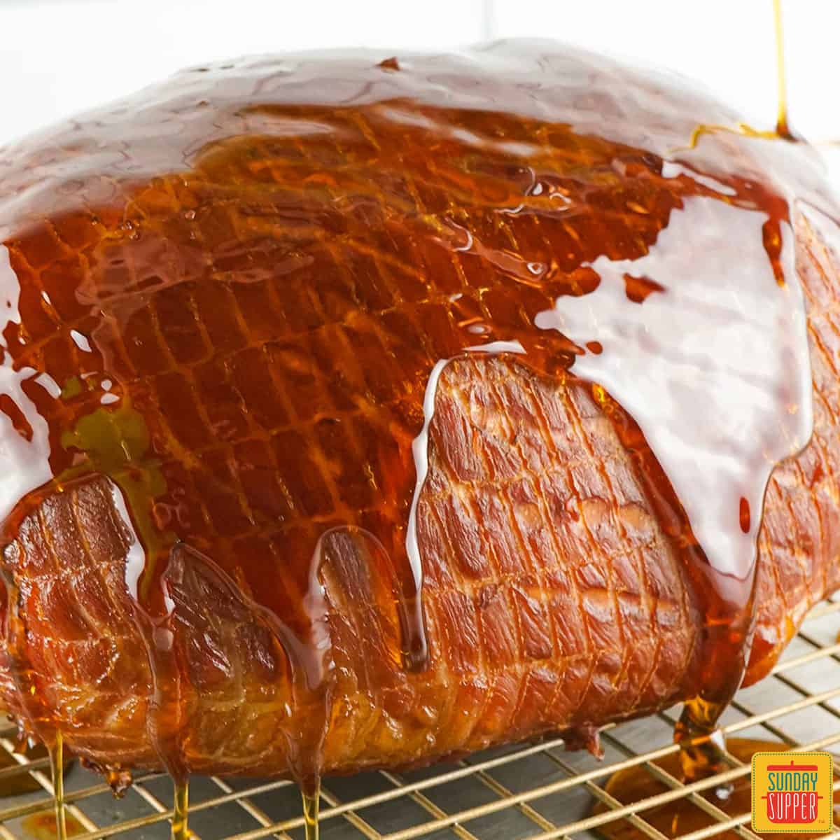 a closeup of a ham with bourbon glaze being poured over it and dripping off into a pan