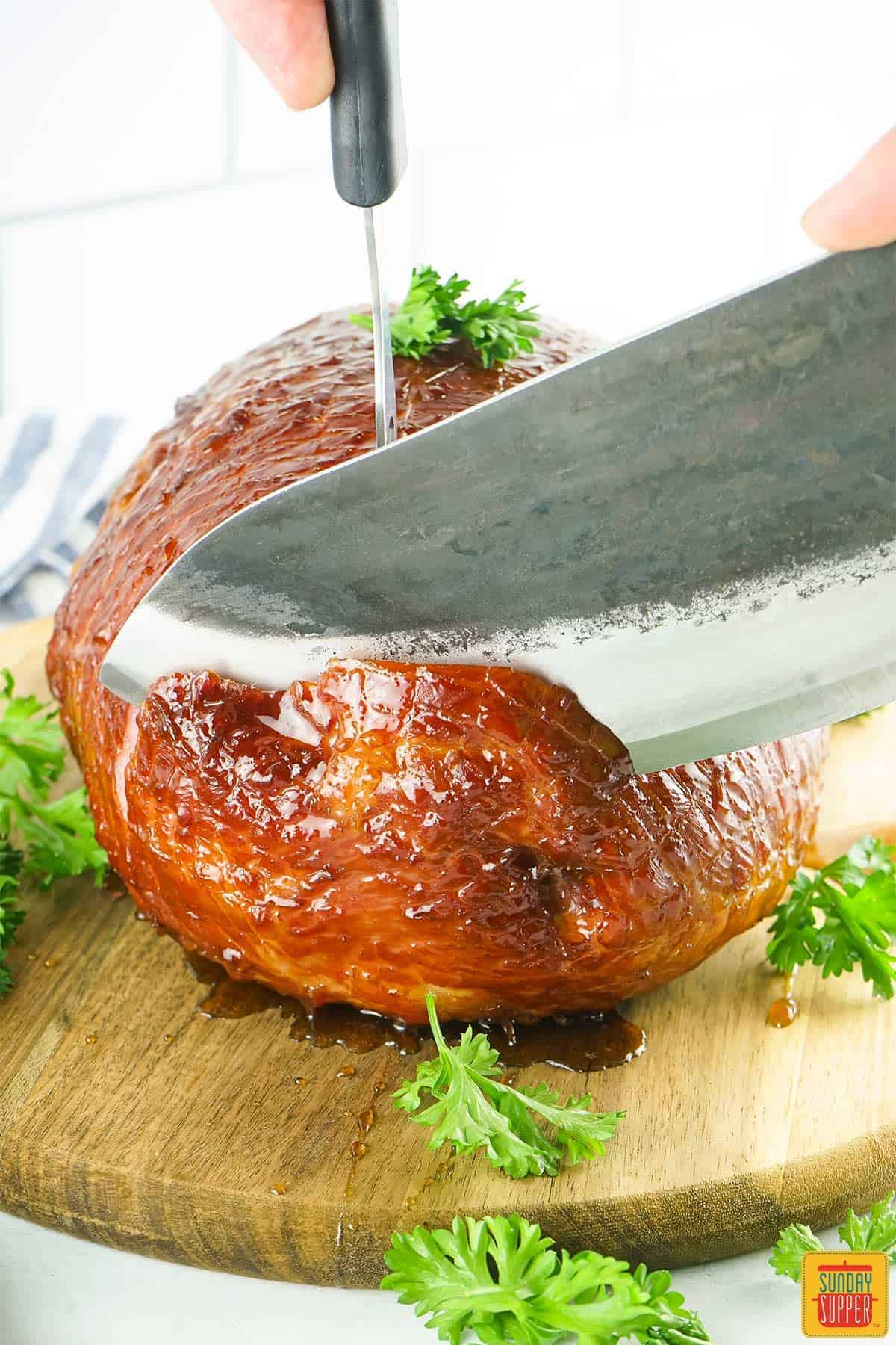 a glazed ham being sliced with a sharp knife on a cutting board