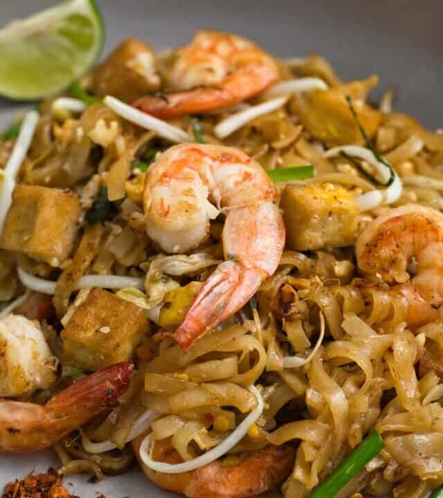shrimp pad thai on a plate up close with red pepper flakes to the side