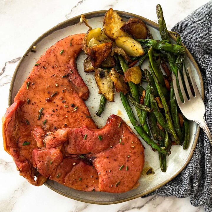 a dinner plate filled with ham steak, sauteed green beans, and roasted potatoes