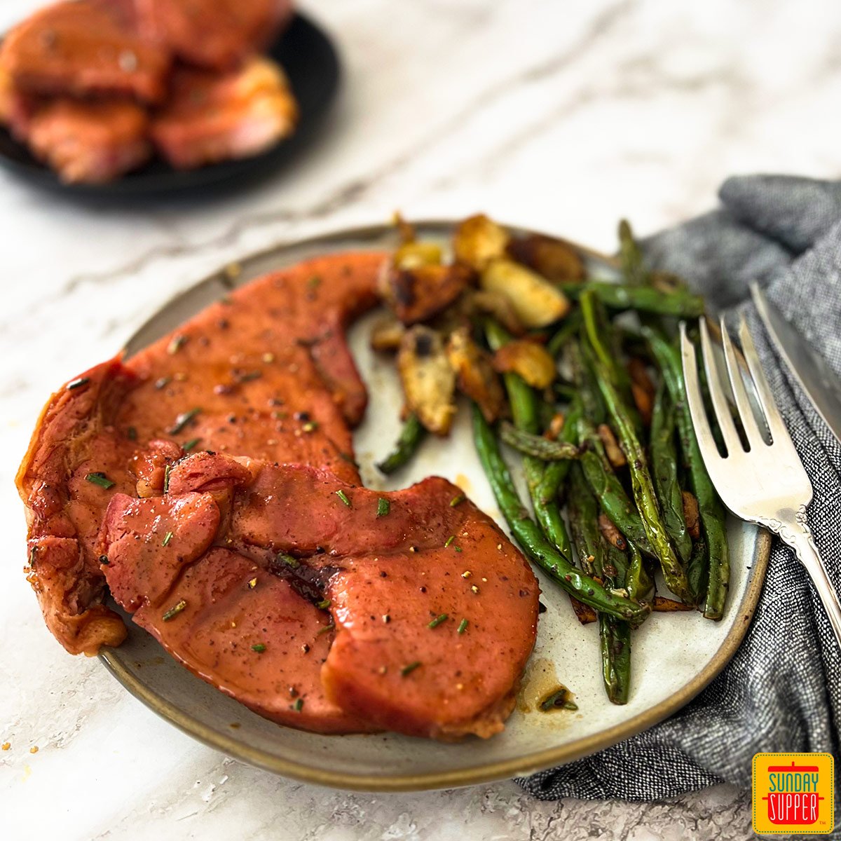 a plate of ham steak, green beans and roasted potatoes with a fork and cloth