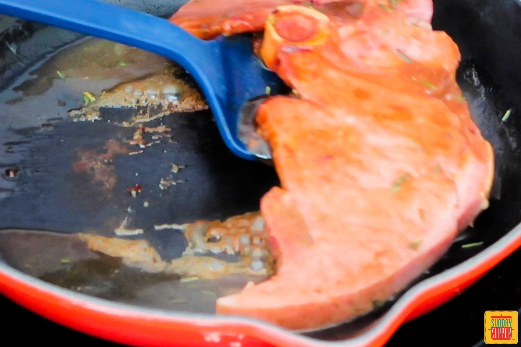 a ham steak being removed from the pan with a spatula