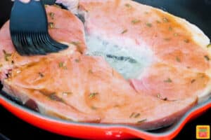 ham steaks in a pan being brushed with glaze