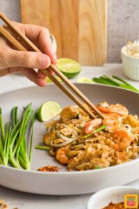 using chopsticks to lift shrimp from pad thai on a plate