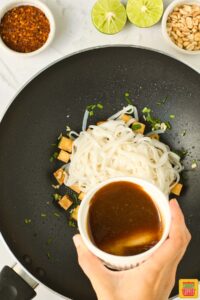 adding sauce to wok with rice noodles and tofu