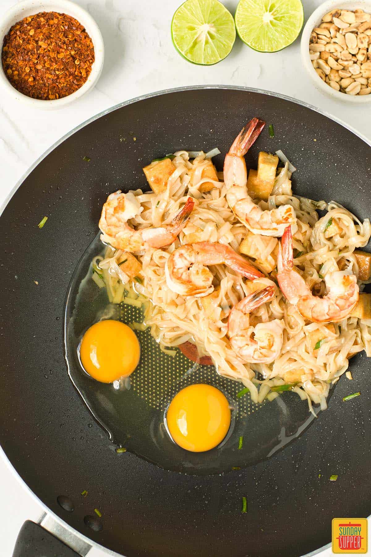 adding eggs to wok with noodles and shrimp