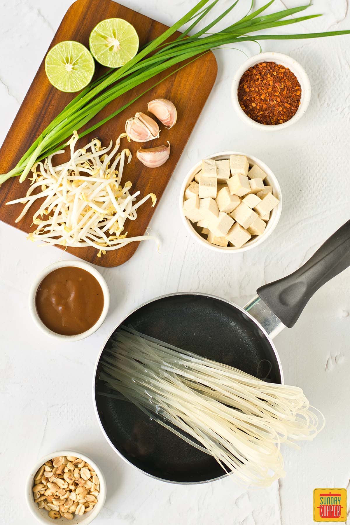 rice noodles cooking in water next to cutting board with other pad thai ingredients