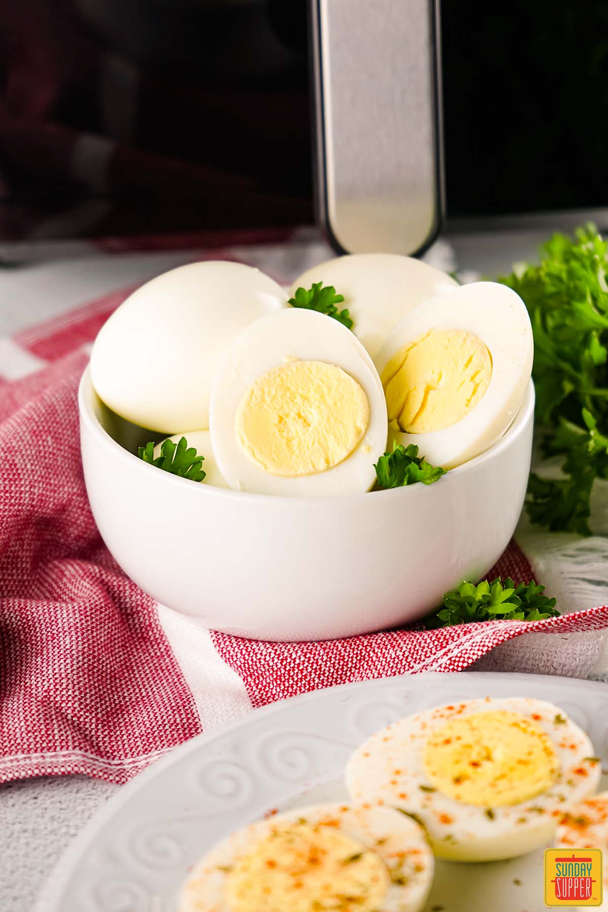 air fryer hard boiled eggs in a white bowl next to a plate of deviled eggs