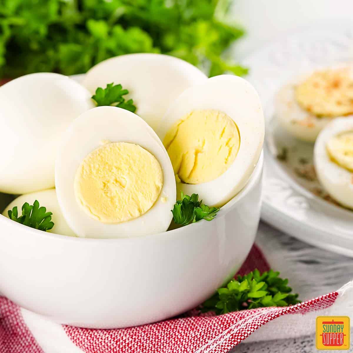 air fryer hard boiled eggs in a white bowl with parsley next to a plate of deviled eggs