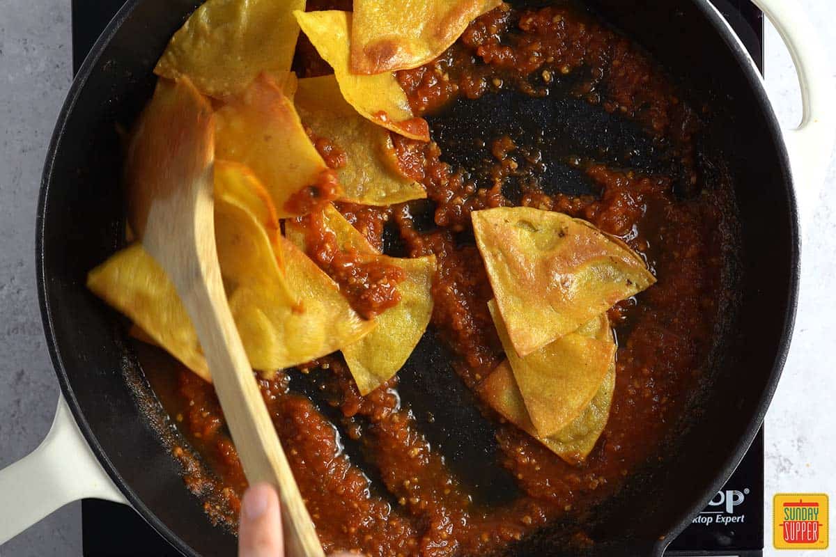 stirring fried tortillas into salsa in a pan
