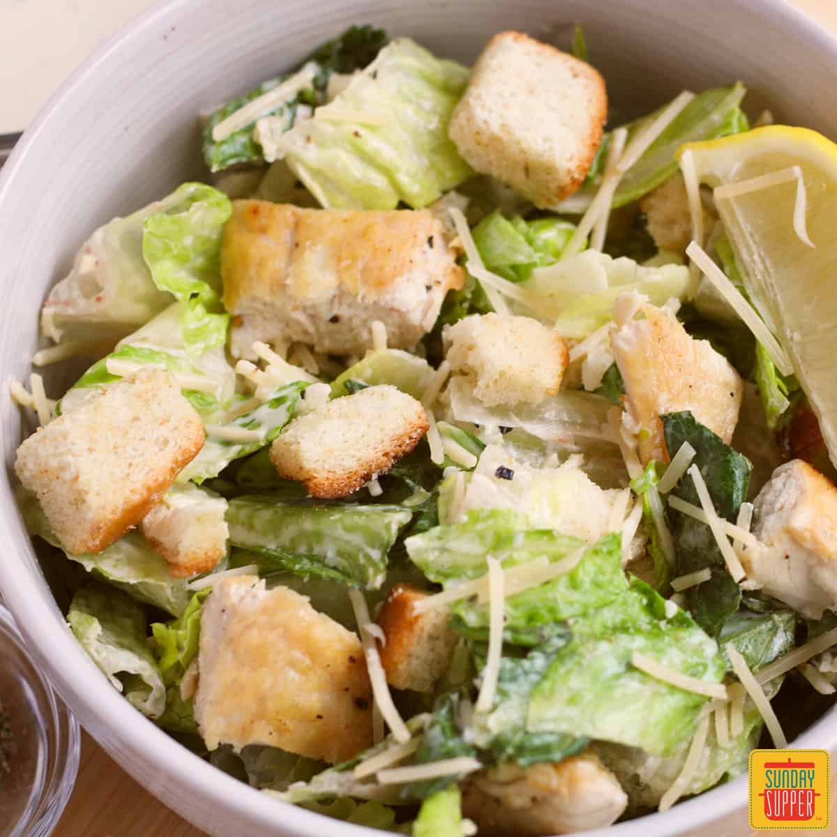 a white dish full of prepared caesar salad with a lemon wedge
