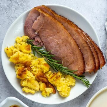 ham sliced on a white plate with herbs and casserole