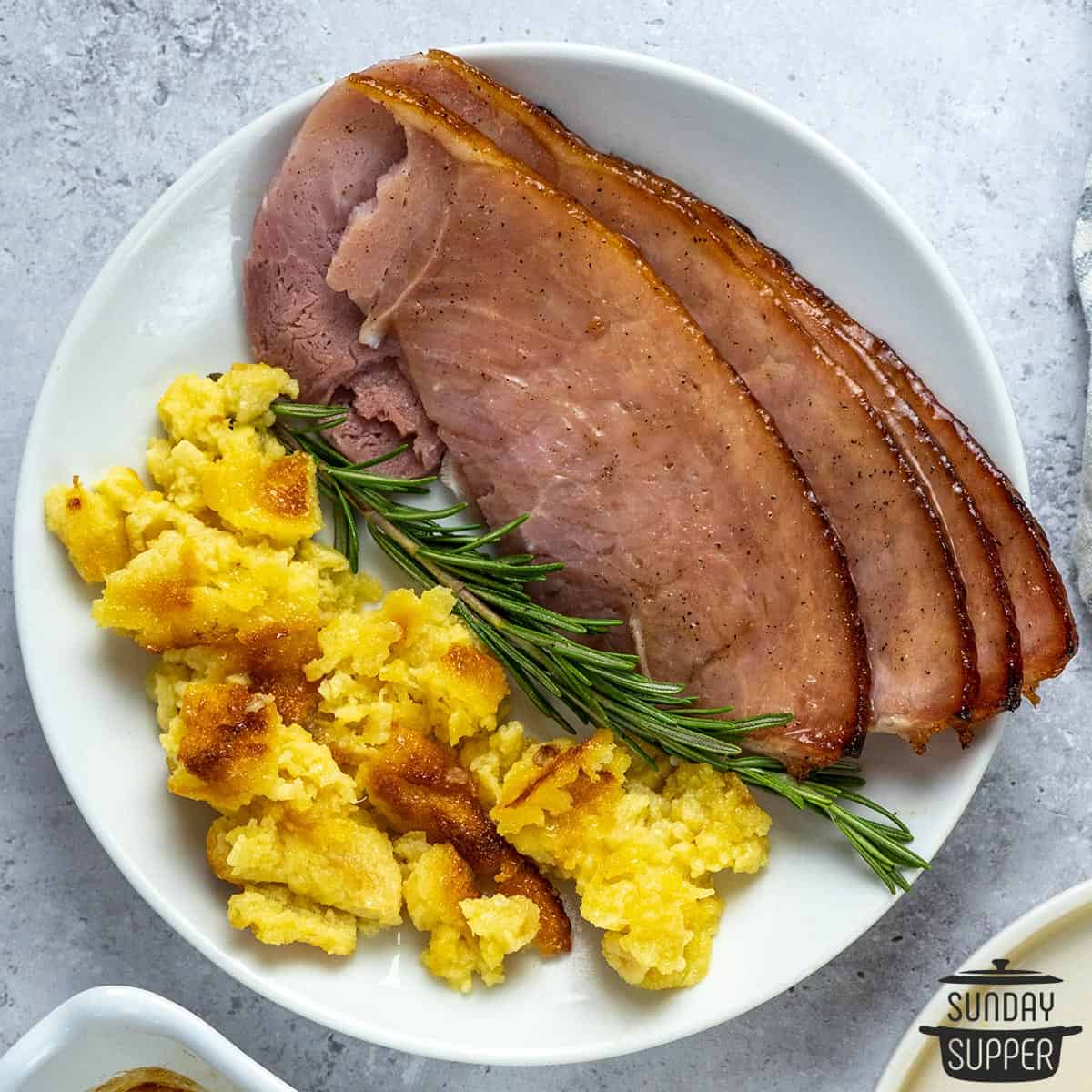 ham sliced on a white plate with herbs and casserole