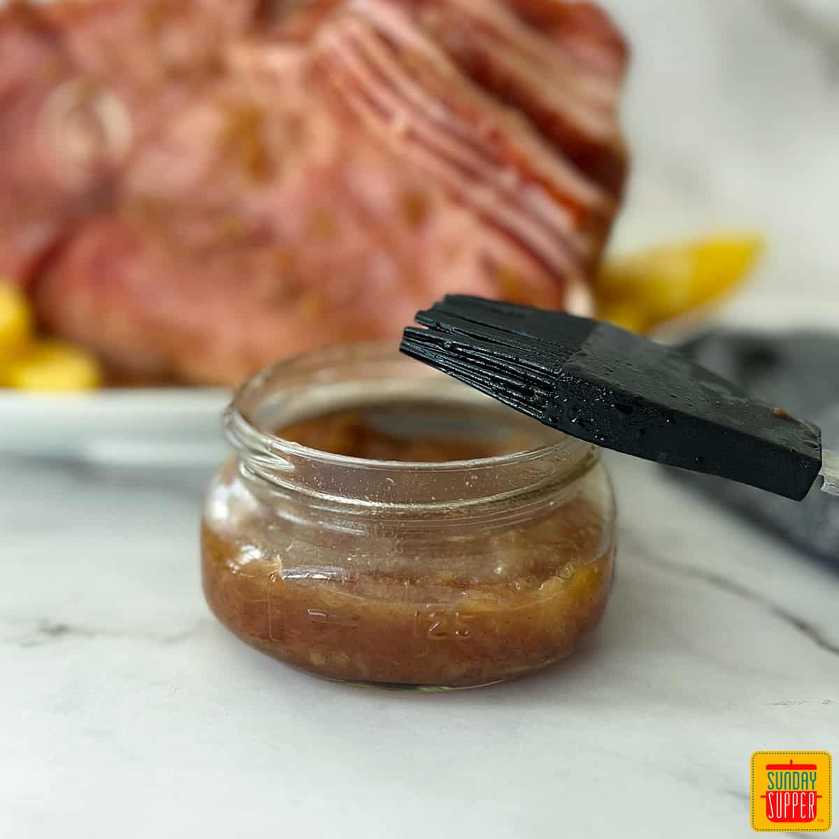 pineapple ham glaze in a clear jar with a basting brush