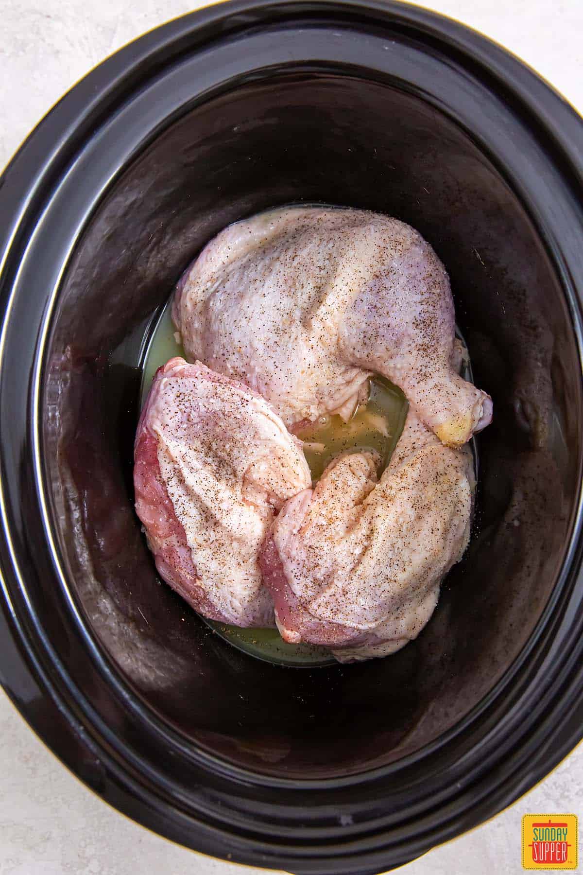 chicken leg quarters added to crockpot with salt and pepper
