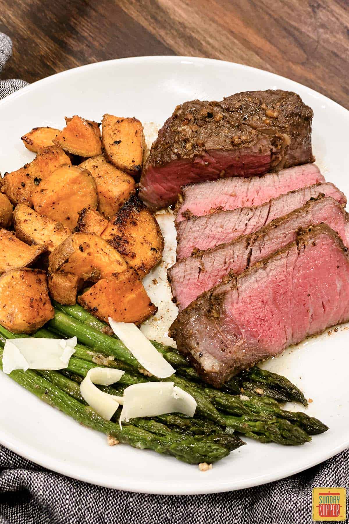 slices of sous vide filet mignon on a white plate with asparagus, sweet potatoes, and freshly grated parmesan