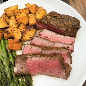 sous vide filet mignon sliced on a plate next to sweet potatoes and asparagus