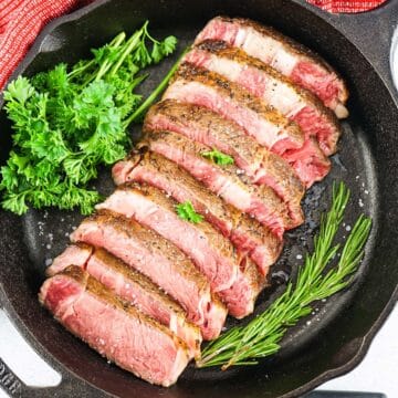 sous vide ribeye steak sliced in a cast iron pan with fresh herbs in the pan